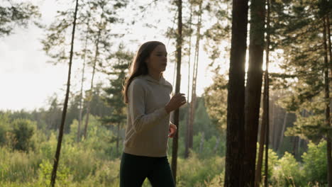 woman athlete runs in woods at sunset. young lady performs cardio routine to improve overall well-being in evening. maintaining physical health