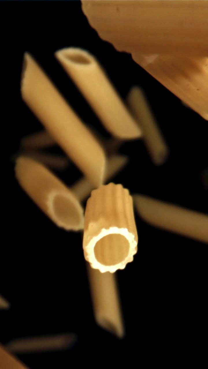 Pasta penne secca che cade al rallentatore su sfondo nero