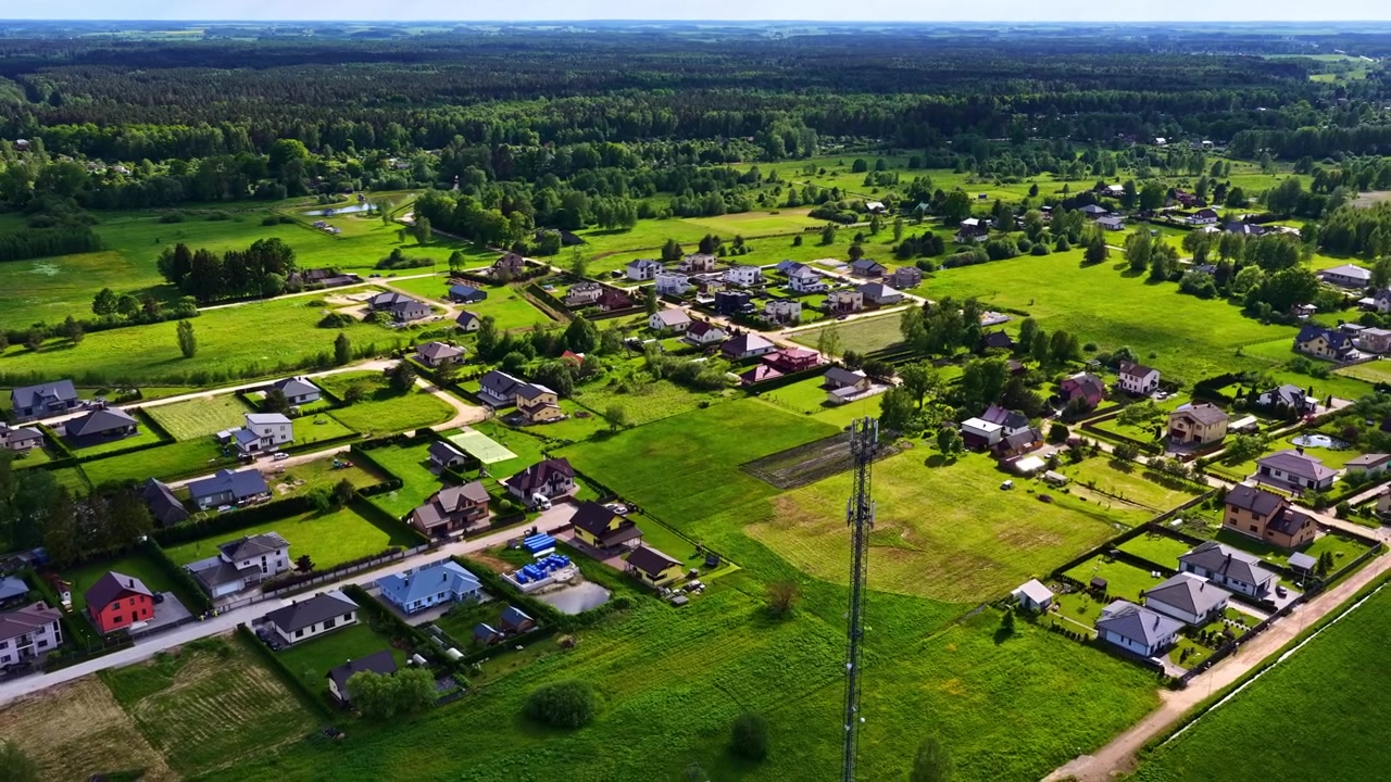 Drone pan shot over modern residential houses surrounded by green fields and a dense forest.