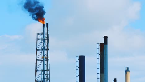 slow motion shot of fire and black, polluting smog pouring out from the top of an industrial refinery into a clear blue sky in curacao