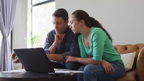 una joven pareja caucásica hablando y pagando sus cuentas usando una computadora portátil