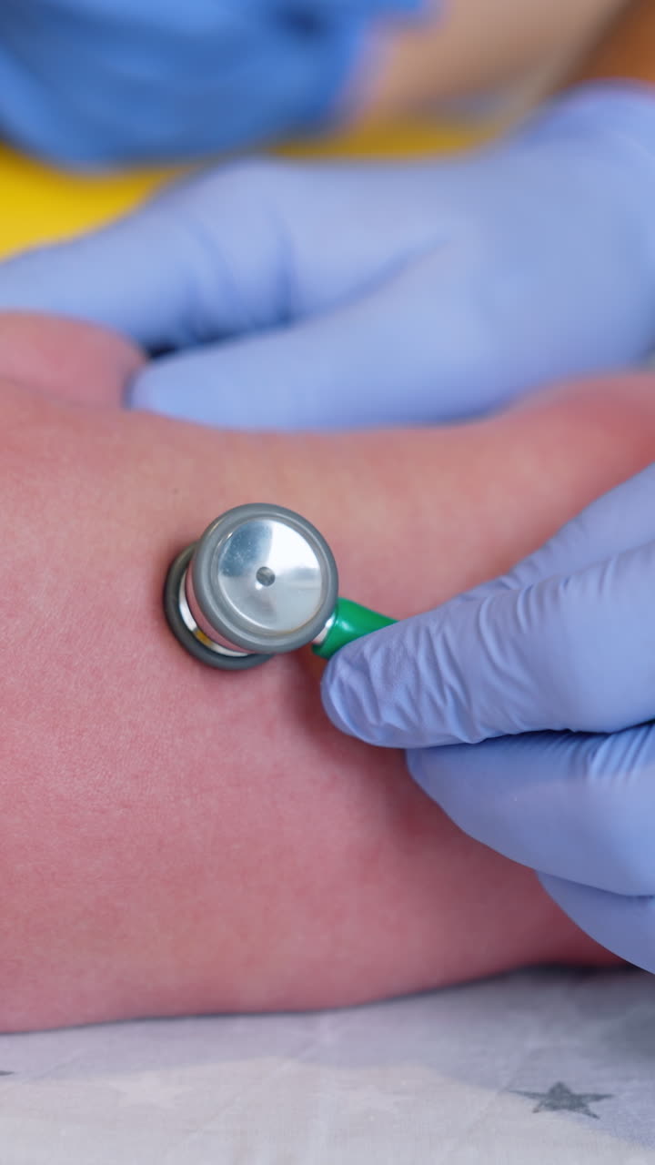 Obstetrician's hands in gloves using stethoscope to examine newborn. Doctor attaches medical device to a child's back. Close up. Vertical video