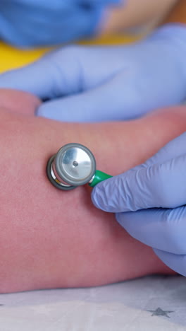 obstetrician's hands in gloves using stethoscope to examine newborn. doctor attaches medical device to a child's back. close up. vertical video