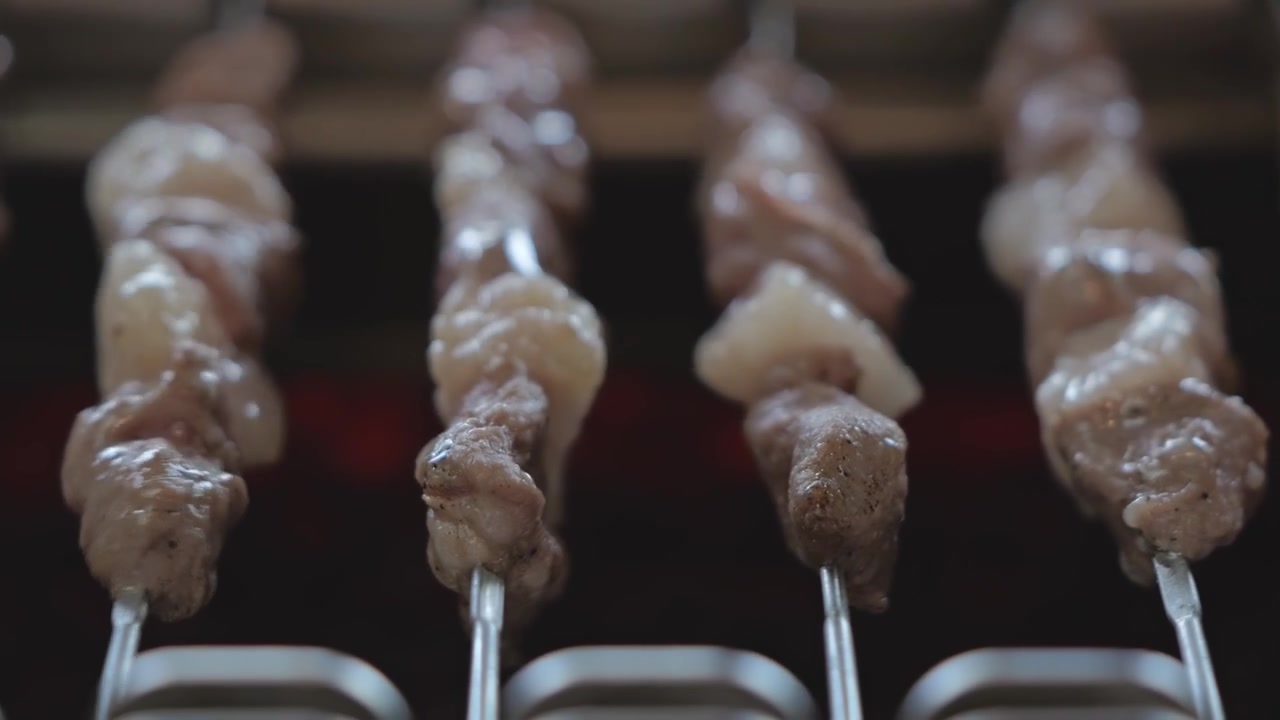 Primo piano di spiedini per barbecue che ruotano lentamente su carboni ardenti su una griglia automatica, catturando cibo che sfrigola, fumo e una texture grigliata appetitosa.