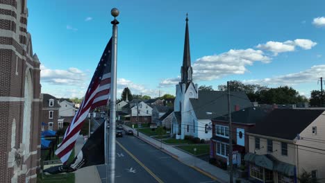 Bandera-Americana-Y-Banderas-De-Pow-Mia-Ondeando-En-Una-Pequeña-Ciudad-De-Estados-Unidos-Con-El-Campanario-De-La-Iglesia