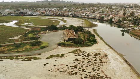 An-aerial-view-flying-over-a-set-of-oceanfront-oil-pumpjacks-with-beachfront-houses-nearby