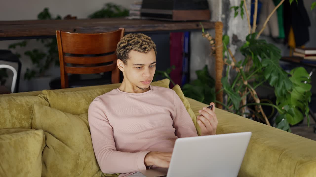 Diverse raced man shopping with a credit card and laptop in and apartment
