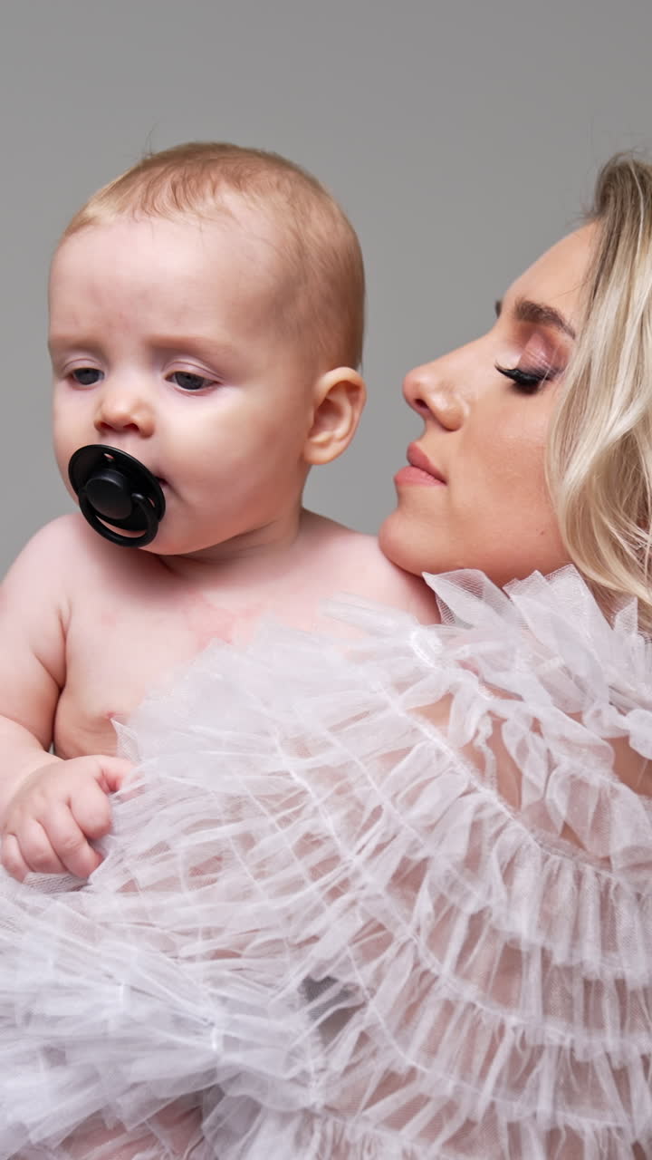 Caucasian woman stands her back to camera holding a baby. Little infant in mom's hands having a pacifier in mouth. Vertical video