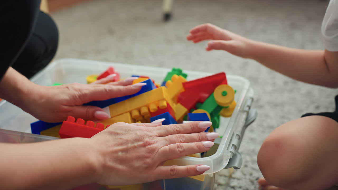 Parent and child building together. Mother and her son engaging in constructive play with blocks. Loving mother and young boy assembling colorful bricks on floor with gentle instruction