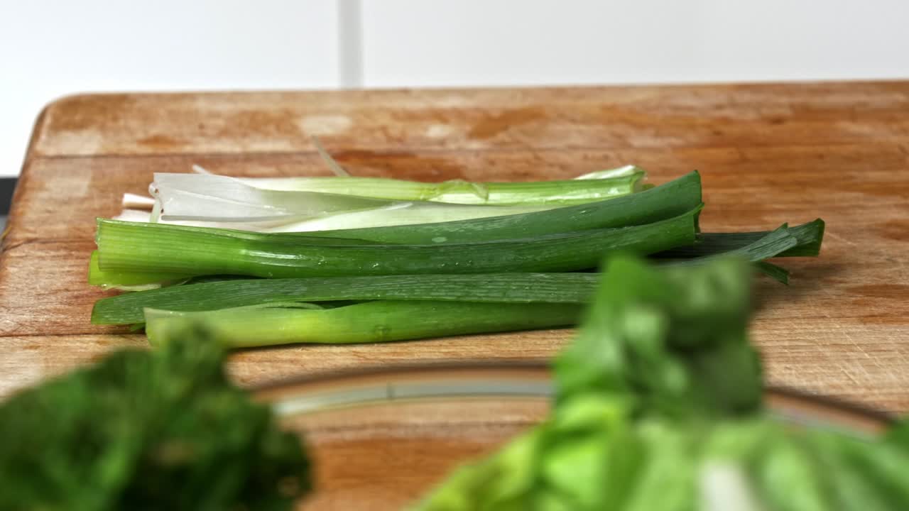 Green onions prepped on a wooden cutting board with a bowl of broccoli in the foreground