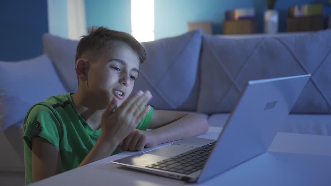 un niño haciendo una videollamada en una computadora portátil soplando el corazón a la cámara.