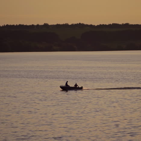 motor boat floating in water on the forest background at dusk. two people in a boat swimming along the river in the evening.