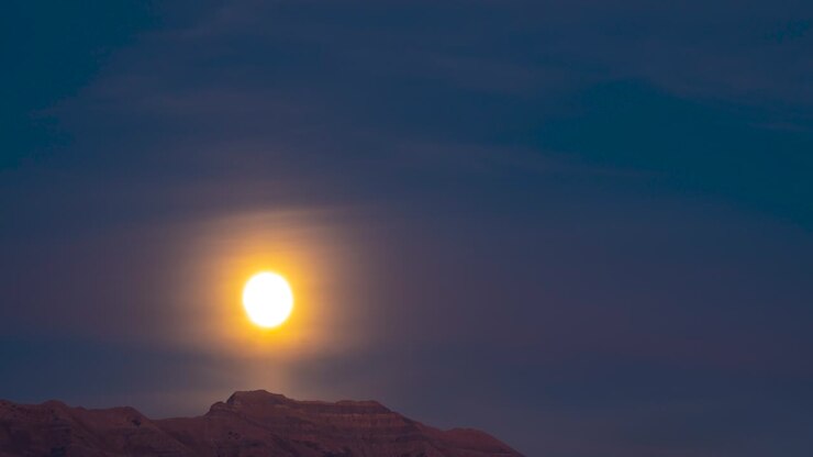 Sunset to nightfall with the glowing full moon rising above the mountain peak - time lapse
