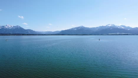 Malerischer-Tiefflug-über-Bayerns-Berühmtestem-Chiemsee-In-Ländlicher-Umgebung-Mit-Einem-Wunderschönen-Himmel,-Klarem-Blauem-Wasser-Und-Den-Atemberaubenden-Alpenbergen-Im-Hintergrund-An-Einem-Sonnigen-Tag