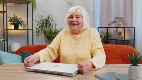 senior grandmother woman sits on sofa closing laptop pc after finishing work in office room at home