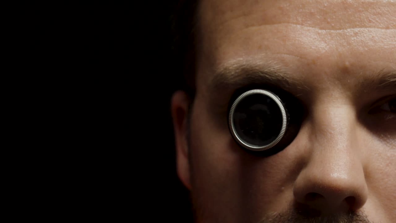 A person inspects a small object using a magnifying monocle, showing precision work and careful observation in a detailed close-up shot