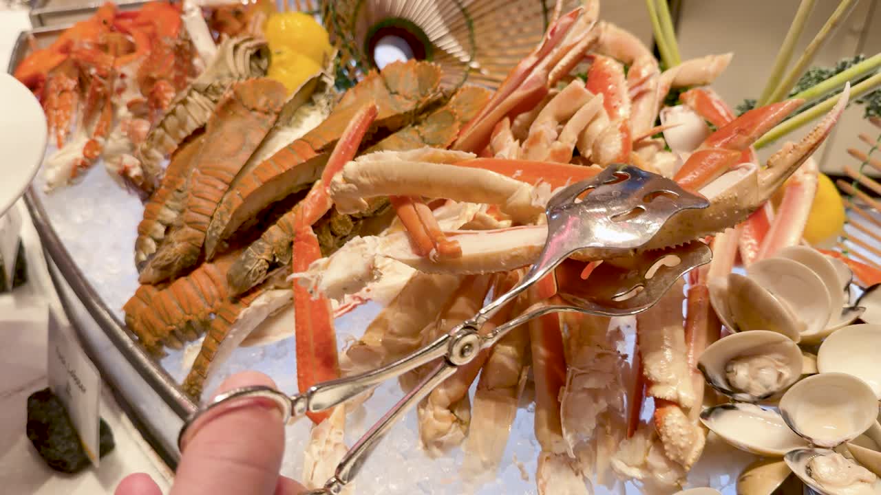 Close-up shot of metal tongs selecting king crab legs from a chilled ice seafood display