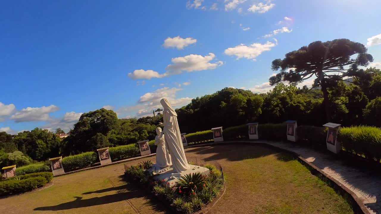 Orbital view of Our Lady of Caravaggio and Giovannette Marble Statue in a beautiful garden in a sunny day followed by escape towards church (slow motion 50FPS)