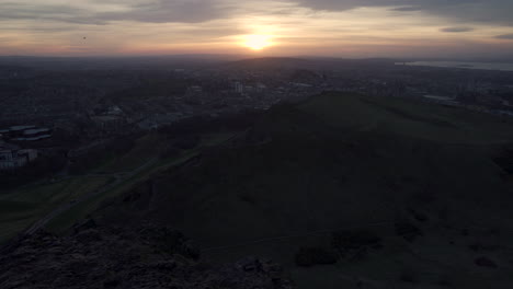 Pedestal-revealing-shot-of-whole-city-of-Edinburgh-from-arthurs-seat-mountain-from-above-during-a-wonderful-sunset-with-epic-skyline