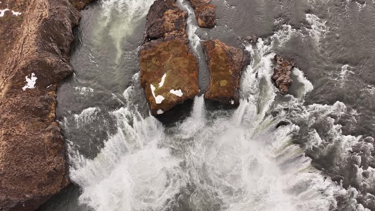 Rushing water over rocky terrain with snow patches, aerial view of a waterfall