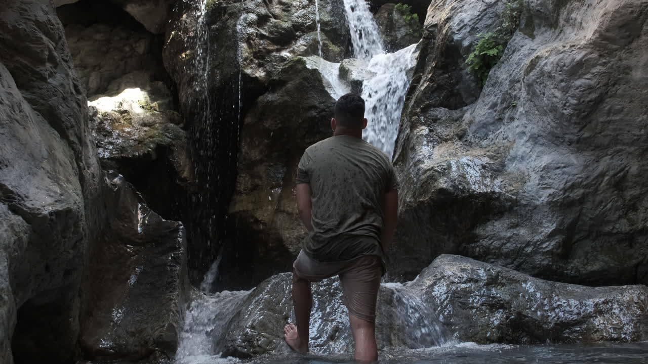 A man standing in a rocky gorge, looking at a waterfall