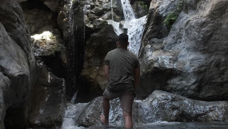 a man standing in a rocky gorge, looking at a waterfall