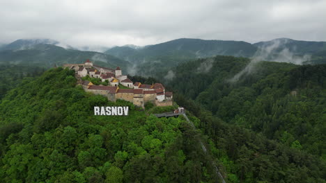 majestic rasnov citadel perched atop a hill, surrounded by lush green forest, in a cloudy day