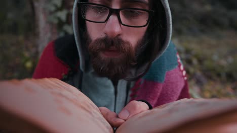 young man with long beard in glasses is reading book with checkered blanket on a rainy weather