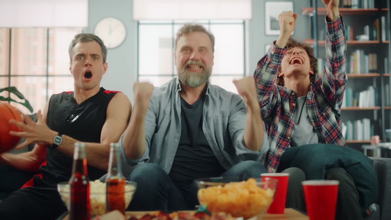 en casa, tres alegres fanáticos del baloncesto sentados en un sofá miran el juego en la televisión, celebran la victoria cuando el equipo deportivo gana el campeonato. un grupo de amigos aplauden cuando los favoritos juegan. retrato ancho