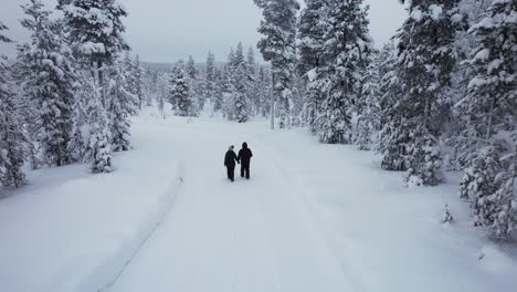 drone follows couple walking together exploring in snowy forest in lapland, finland, arctic circle