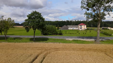 Slow-aerial-forward-flight-showing-empty-road,farm-building-and-forest-in-background
