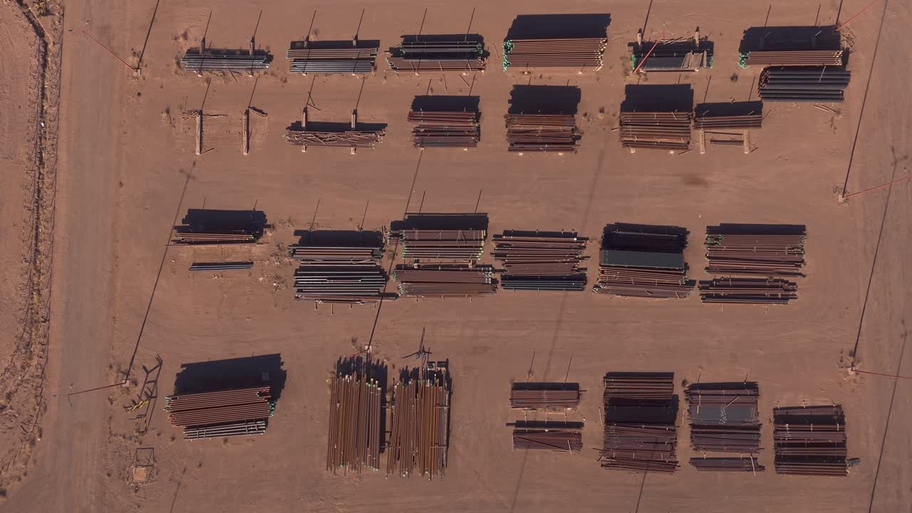 Top-down aerial view of an oil and gas industrial facility showing logistics areas, stored materials, road infrastructure, and operational layouts within a desert environment