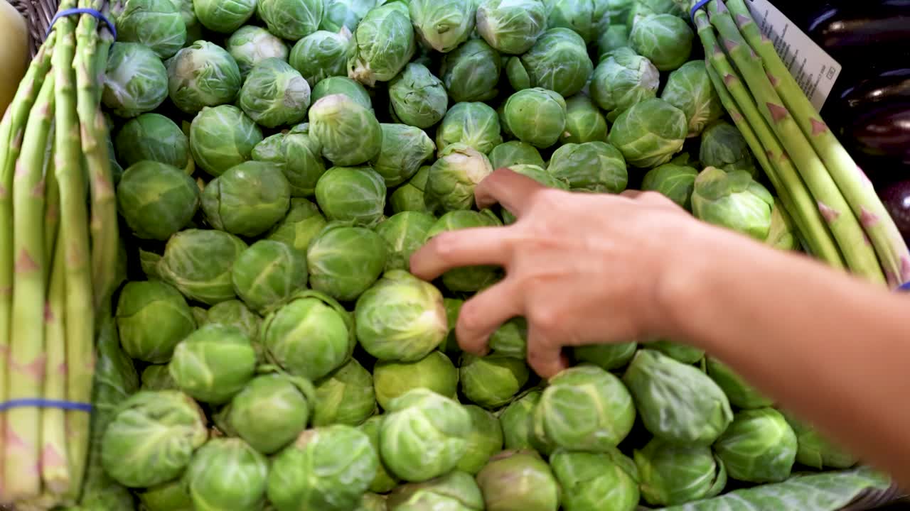 A hand selects fresh Brussels sprouts from a supermarket display, highlighting vibrant greens and natural lighting