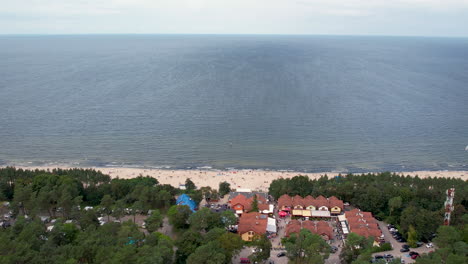 Aerial-shot-of-a-coastal-area-with-a-sandy-beach-in-Stegna,-blue-waters,-and-a-bordering-tree-line