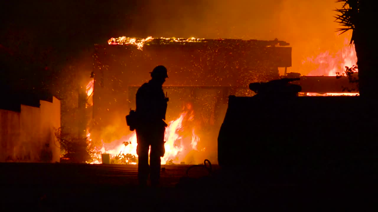 A hero firefighter walks in front of a burning building as it collapses