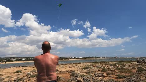 back view of man holding toy kite on beach on summer sunny day