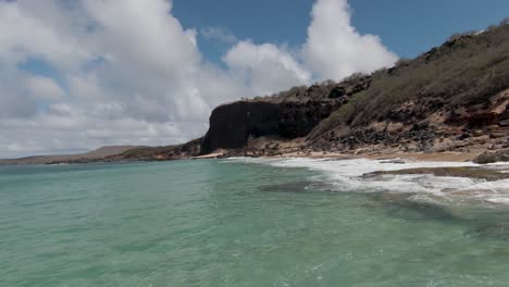 aerial slow motion view of ocean waves crash on molokai, hawaii shoreline. valley tropical environment establishing shot with white sand and turquoise water