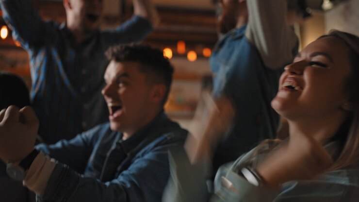 Crowd of spectators cheering at sports event man and woman holding a glass of beer. football team supporters actively jumping and chanting in crowd.