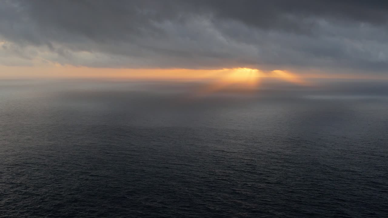 Sunset over ocean with dark clouds above, high point view