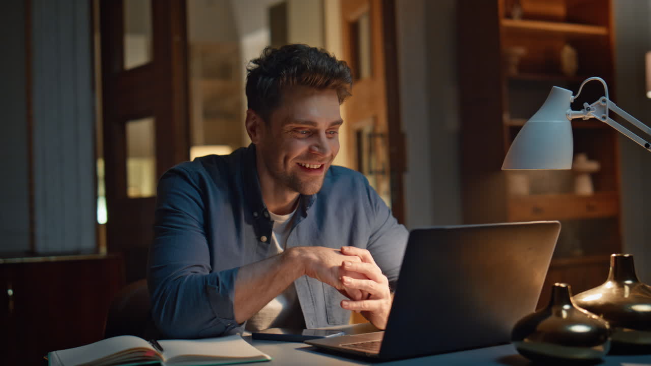 Specialista della risata che si diverte a fare videoconferenza con il portatile seduto da solo nell'appartamento in primo piano
