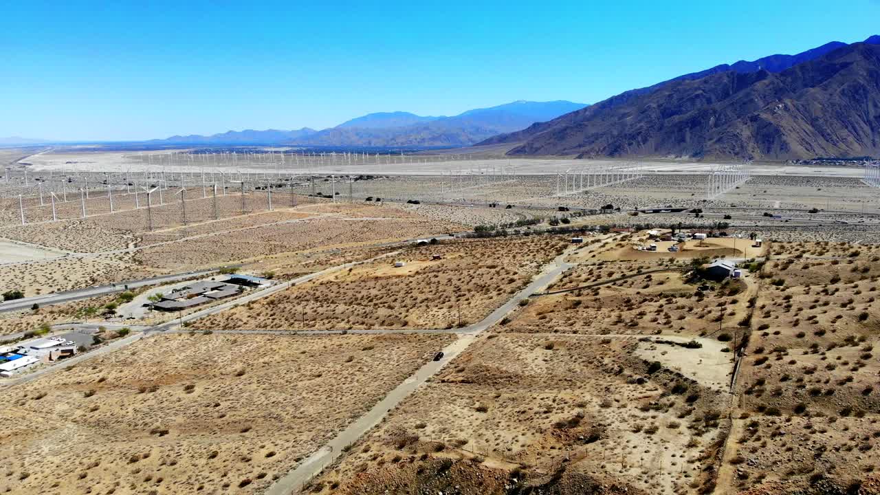 Fly in across barren desert with windmills, wind turbines energy, green, renewable, huge power generating farm and Palm Springs in distance, aerial 4k drone, Coachella Valley, Cabazon, California
