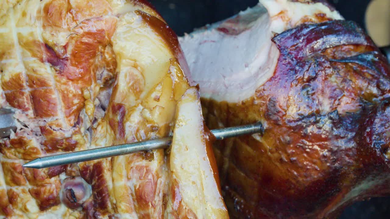 Juicy pork knuckle rotates on spit, slow-roasting over wood fire in outdoor market setting