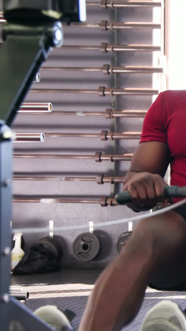 Vertical video: Grabbing rower handle, man in red shirt, black shorts rowing at gym for cardio