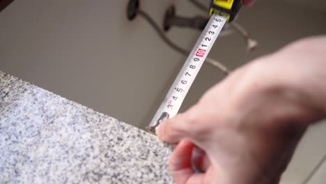 el hombre utiliza cinta métrica de acero para medir el tamaño de la encimera en la cocina - cerrar