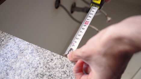 man uses steel tape measure in measuring size of countertop in the kitchen - close up