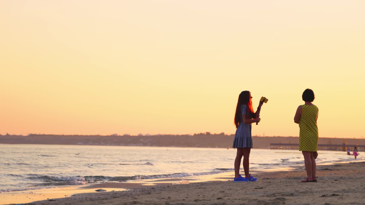 Pretty girl in sunglasses taking photo of herself on the sea background. Evening landscape on the sea shore and women standing at sunset.