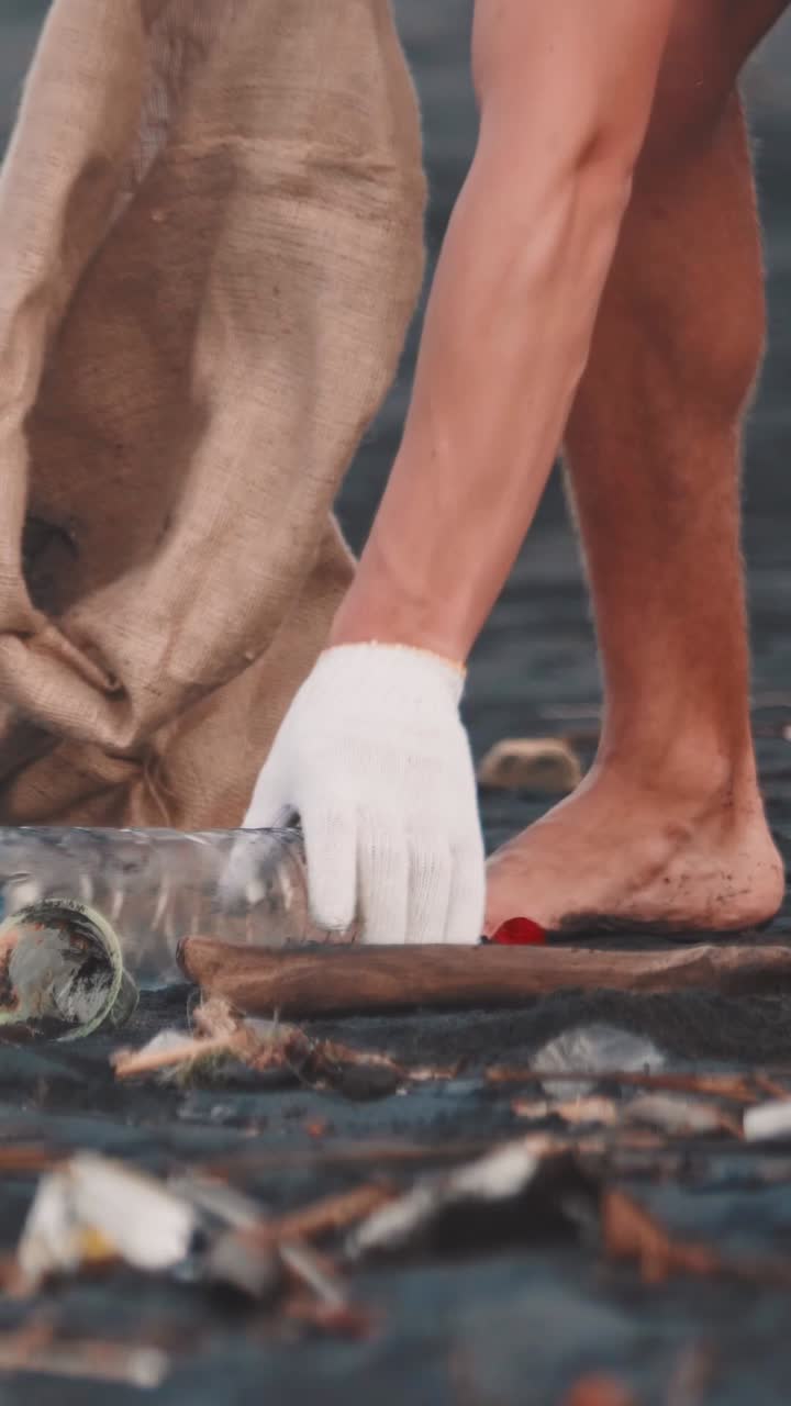 Hands of volunteer picking up trash from ground and throwing it into bag