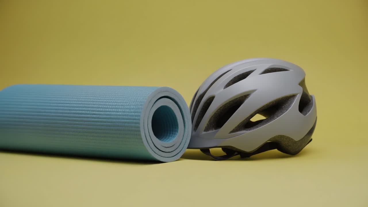 Matras Yoga Tergulung di Sebelah Helm Sepeda di Atas Latar Belakang Kuning