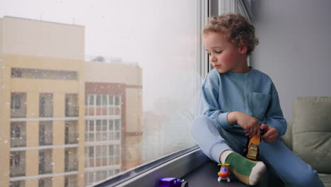 happy four years toddler is sitting calmly on windowsill and looking on street in winter day carefree childhood