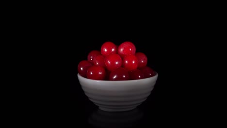 pile of red ripe cherries in small white cup revolves on black background.